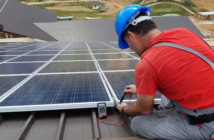 Instalator montuje panel fotowoltaiczny na dachu domu jednorodzinnego.